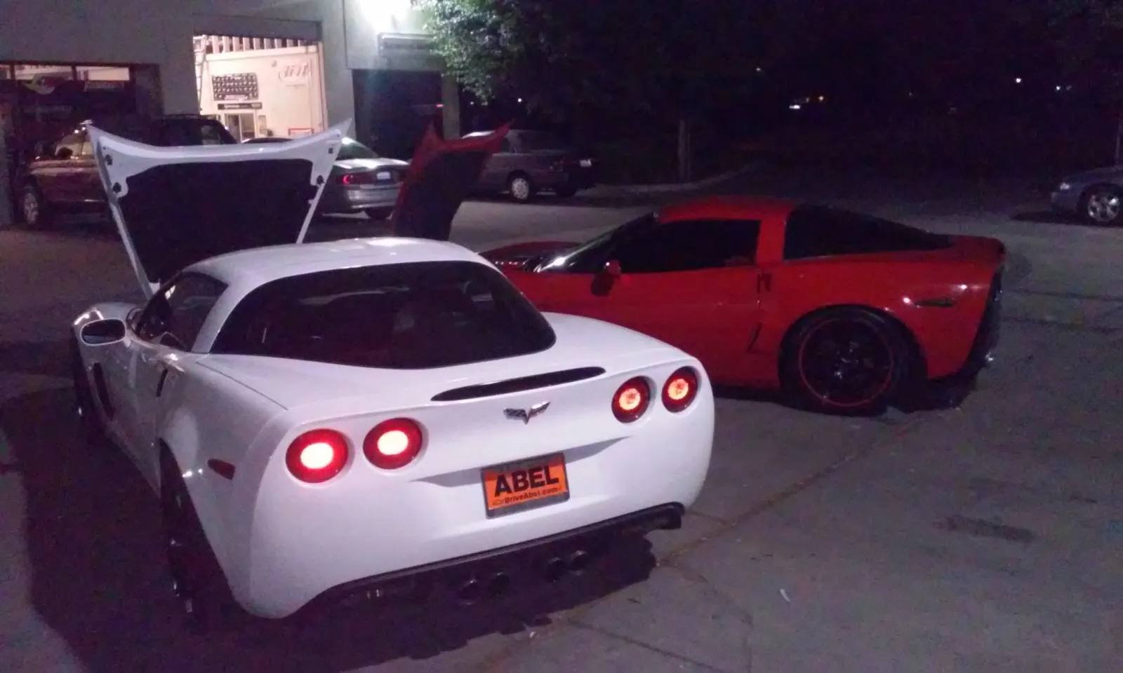 White and red Corvettes parked outside the shop at night